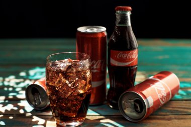 Minsk, Beyaz Rusya-Ağustos 25, 2016. Can ve buzlu Coca-Cola ahşap bir masa üzerinde bir bardak