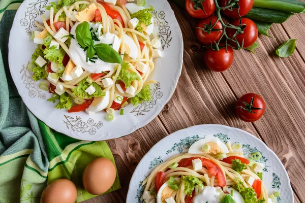 Салат из спагетти с помидорами, салатом, яйцом, сыром Фета, зеленым луком и сметаной — стоковое фото