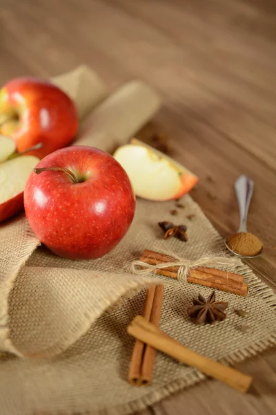 Apples and cinnamon on jute fabric and wooden background — Stock Photo, Image