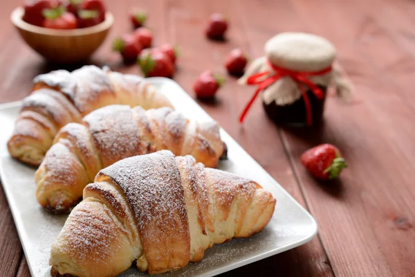 Croissant e una marmellata di fragole sullo sfondo di legno — Foto Stock