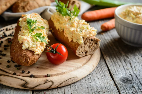 Curd spredes med æg, gulerod, grønne løg, syltede agurk og mayonnaise på en hel hvede baguette - Stock-foto