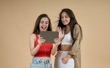 Bej arka planda görüntülü arama için tablet kullanan iki mutlu kadın