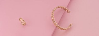 Pembe arka planda altın yüzük ve bilezik.