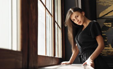 Esmer kadın pencerenin yanında duruyor.