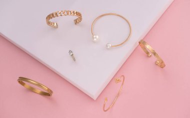 Pembe ve beyaz arka planda modern altın bilezikler koleksiyonu