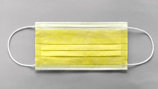 Gri arkaplanda tıbbi koruyucu sarı maskenin üst görüntüsü — Stok fotoğraf