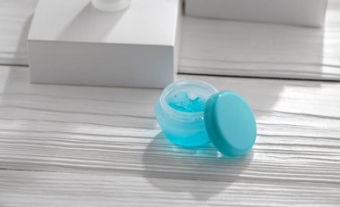 Pencerenin yanındaki ahşap beyaz masada mavi jel kabını aç