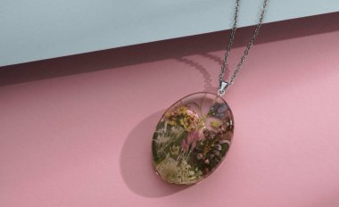 Epoxy Resin necklace pendant with natural flowers inside on pink and blue background clipart