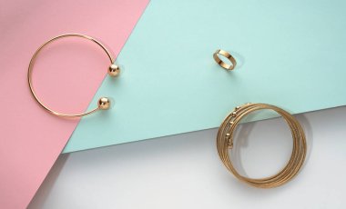 Altın bileziklerin üst görüntüsü ve pastel renkli kağıtların arka planında halka