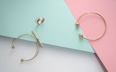 Altın bileziklerin üst görünümü ve pembe ve mavi geometrik arkaplan üzerinde halka kopyalama alanı ile