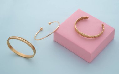 Pembe ve mavi arka planda üç modern altın bilezik koleksiyonu