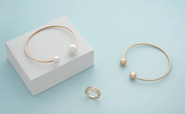 Altın ve inci bilezikler ve mavi arkaplanda beyaz küpte yüzük