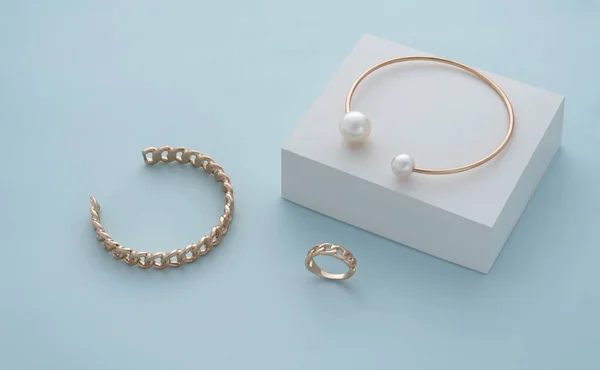 白色盒子上的金珍珠手镯和蓝色背景上的金链状手镯和戒指 — 图库照片