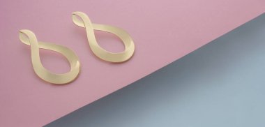 Modern altın sonsuzluk şekilli küpeler pembe ve mavi arka planda fotokopi alanı ile