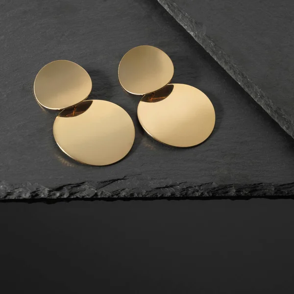 Nowoczesne okrągłe złote kolczyki na ciemnych kamiennych talerzach — Zdjęcie stockowe
