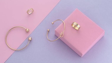 Pembe ve mor pastel arka planda modern altın aksesuarların üst görünümü