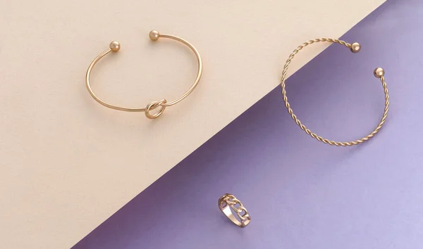 Modern design spiral and knot shape golden bracelets and ring on beige and purple paper