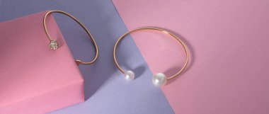 Pembe zemin üzerinde değerli taşlar olan altın bilezikler ve kopyalama alanı olan mor zemin