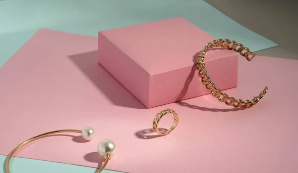 Золотой браслет в форме цепочки и кольцо на розовой коробке на зеленом фоне бумаги с копировальным пространством — стоковое фото
