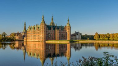 Frederiksborg Şatosu, güneş doğduktan hemen sonra gölün yansımasında ve ön planda biraz sazlık, Hillerod, Danimarka, 17 Ekim 2020