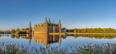 Frederiksborg Şatosu, güneş doğduktan hemen sonra gölün yansımasında ve ön planda biraz sazlık, Hillerod, Danimarka, 17 Ekim 2020