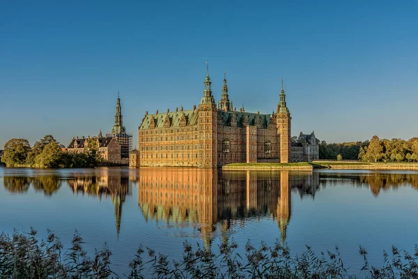 Frederiksborg Şatosu, güneş doğduktan hemen sonra gölün yansımasında ve ön planda biraz sazlık, Hillerod, Danimarka, 17 Ekim 2020