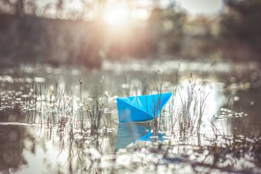 paper boat floating on calm reflective water surface, symbol of childhood imagination, freedom and tranquility