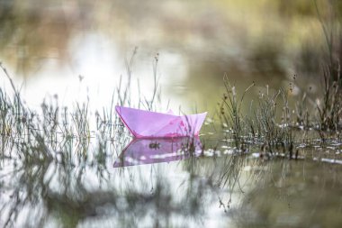 paper boat floating on calm reflective water surface, symbol of childhood imagination, freedom and tranquility
