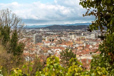 Panoramic view of Graz Austria with red rooftops modern buildings and distant mountains under cloudy sky