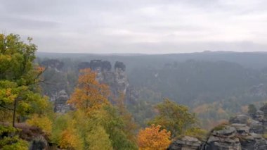 Atmosferik seyahat videosu Almanya 'nın Sakson İsviçre kentindeki ünlü Bastei Köprüsü' nü gösteriyor. Sis, yağmur ve sonbahar renkleri kumtaşı kayalıkları ve orman vadisi üzerinde dramatik bir hava yaratır..