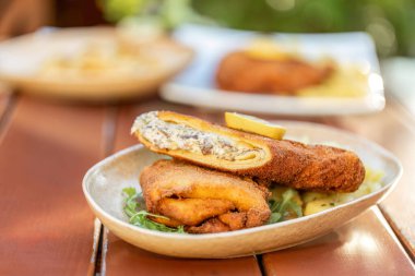 Kremalı mantar karışımıyla doldurulmuş ve limon dilimiyle süslenmiş kırsal bir tabakta servis edilen gevrek vejetaryen cordon bleu 'nun yakın çekimi. Tabak açık havada doğal ışık altında çekiliyor, dokuyu ve tazeliği vurguluyor..