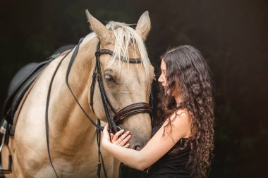 Palomino Kinsky atıyla doğal ışık altında bağ kuran genç bir kadın.