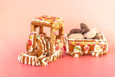 Renkli şekerlemeler ve beyaz kremalarla süslenmiş el yapımı zencefilli ekmek treni, çeşitli Noel kurabiyeleriyle dolu küçük bir arabayı çekiyor, festival tarzı parlak pembe bir yüzey üzerinde sergileniyor.