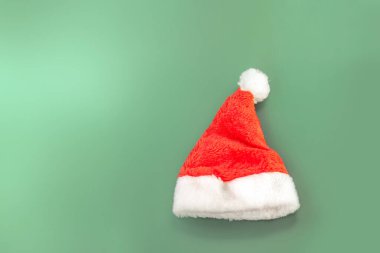 Yeşil arka planda beyaz süslemeli kırmızı Noel Baba şapkası içeren en düşük Noel kompozisyonu. Kopyalama alanı olan şenlikli ve basit bir yerleşim