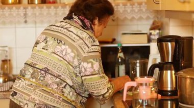 Kıdemli kadın sıcak bir mutfakta çay hazırlıyor, mutfak eşyalarıyla uğraşıyor ve sıcak bir içecek hazırlıyor.