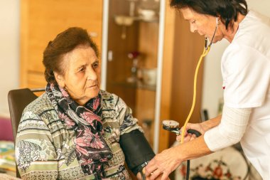 Evde bakım hemşiresi, evde sağlık ziyareti sırasında yaşlı bir kadının kan basıncını ölçer..
