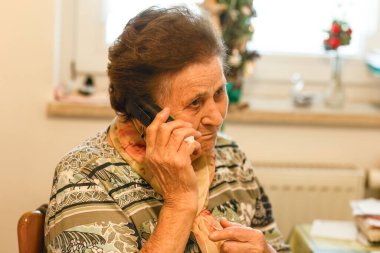 Evde odaklanmış bir şekilde telefonla konuşan yaşlı bir kadın.