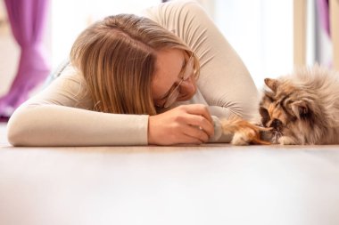 Yerde bir kadının uzun saçlı kedisiyle şakalaştığı, sıcaklığını ve günlük bağlarını gösteren rahat bir sahne..