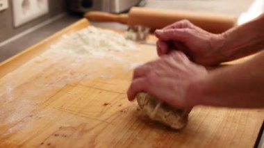  Elleri ahşap tahtada hamur yoğururken arka planda un gerçek ev yapımı pişirme anını gösteriyor.