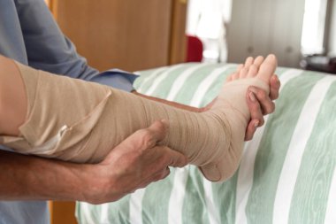 Bakıcı, hemşire eğitiminde sıkıştırma terapisi uygularken hasta mankeni üzerindeki sıkıştırma bandajını inceler.