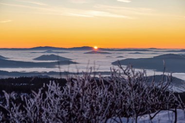 Sis dolu vadiler ve karlı orman tepeleri üzerinde altın şafak ışığı. Korunmuş ulusal park arazisindeki dağ zirvelerinden görülebiliyor.