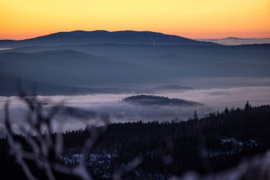 Sis dolu vadiler ve karlı orman tepeleri üzerinde altın şafak ışığı. Korunmuş ulusal park arazisindeki dağ zirvelerinden görülebiliyor.