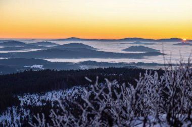 Sis dolu vadiler ve karlı orman tepeleri üzerinde altın şafak ışığı. Korunmuş ulusal park arazisindeki dağ zirvelerinden görülebiliyor.