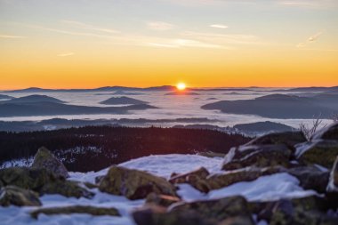Sis dolu vadiler ve karlı orman tepeleri üzerinde altın şafak ışığı. Korunmuş ulusal park arazisindeki dağ zirvelerinden görülebiliyor.