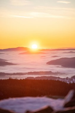 Sis dolu vadiler ve karlı orman tepeleri üzerinde altın şafak ışığı. Korunmuş ulusal park arazisindeki dağ zirvelerinden görülebiliyor.