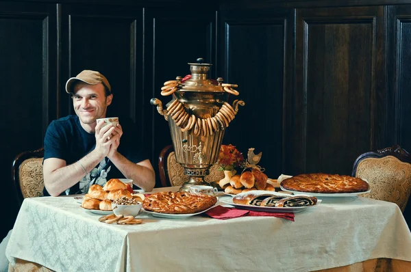 Ein Mann an einem Tisch trinkt Tee aus einem Samowar mit Torten — Stockfoto