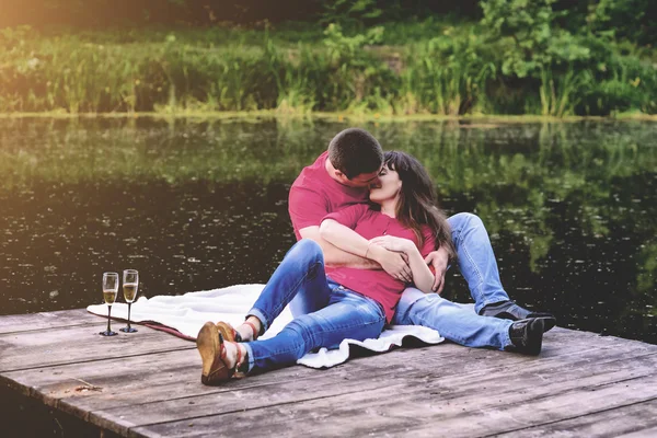 Enamorado de un par de jóvenes sentados en un puente de madera cerca del río. Tonificación — Foto de Stock