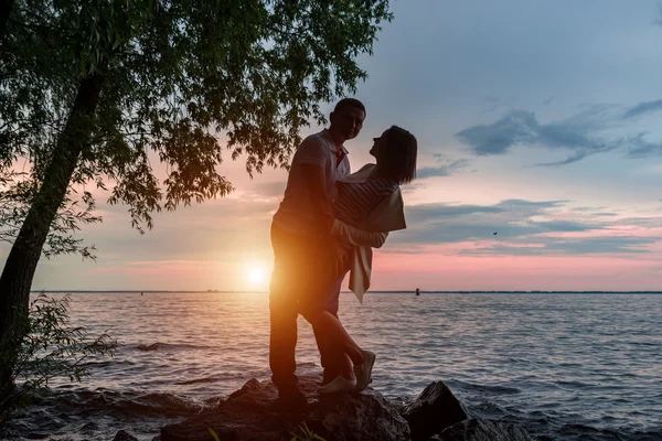 Silueta de una pareja romántica sobre un fondo al atardecer cerca del agua.Tonificación — Foto de Stock