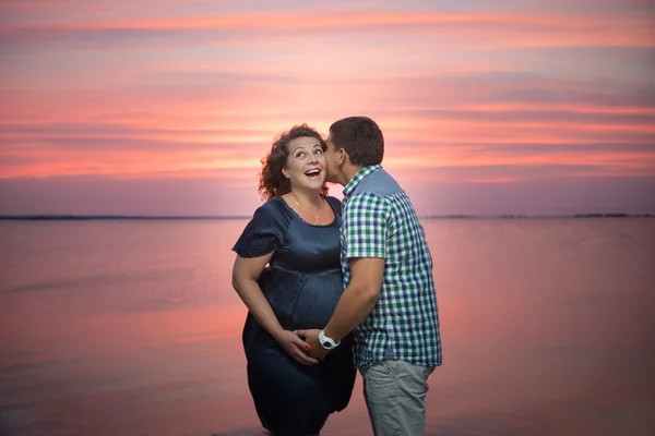 Pareja feliz y alegre cerca del fondo del atardecer del río. La mujer está embarazada. Tonificación —  Fotos de Stock