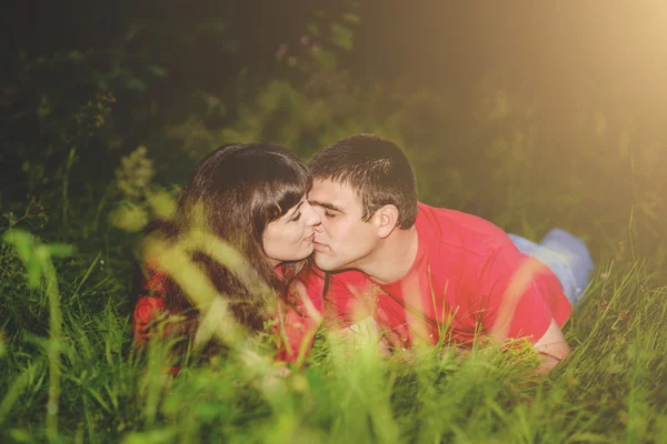 Pareja de enamorados jóvenes en la naturaleza de las camisas rojas se acuestan en la hierba y besan. Tonificación . — Foto de Stock